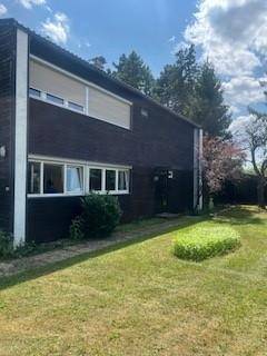 Vorderansicht des Hauses mit dunkler Fassade, großen Fenstern und einem gepflegten Rasenbereich.
