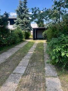 Gepflasterte Einfahrt führt zu einem Carport oder einer Garage, umgeben von üppigem Grün.