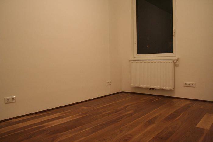 Helles Schlafzimmer mit Holzparkettboden, großem Fenster und Heizkörper, bereit zur Einrichtung.