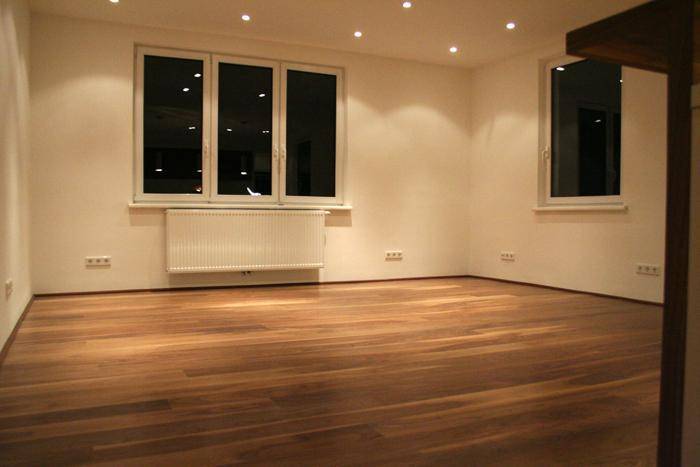 Leeres Wohnzimmer mit großen Fenstern, Holzparkettboden und Heizkörper, bereit zur individuellen Gestaltung.