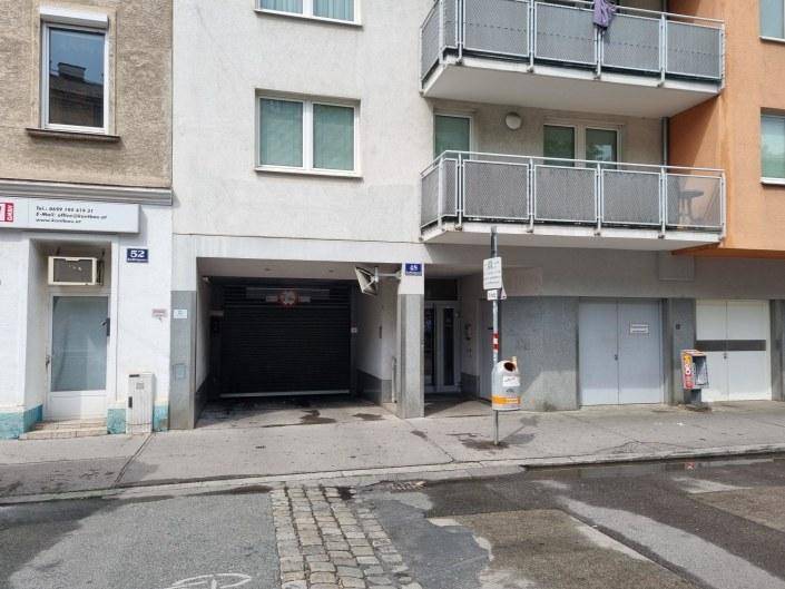 Moderne Fassade eines Wohngebäudes mit Balkonen und der Einfahrt zur Tiefgarage von der Straße aus.