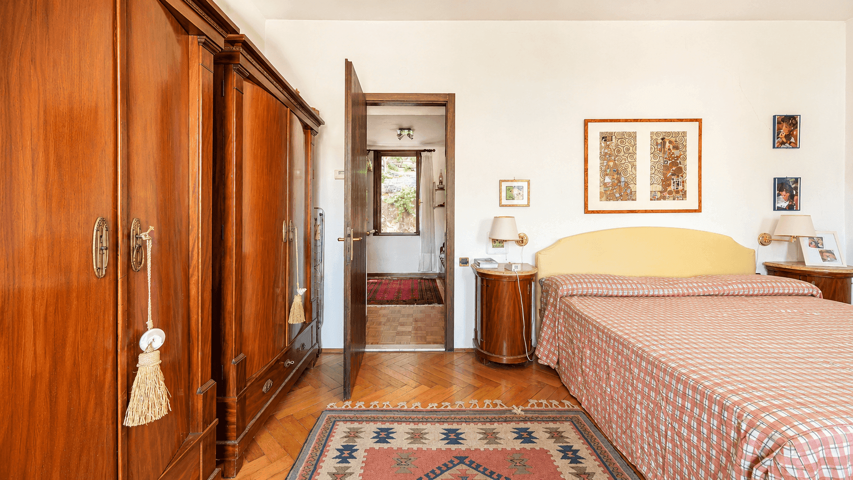 Schlafzimmer mit Parkettboden, großem Holzschrank und Zugang zu einem weiteren Raum.