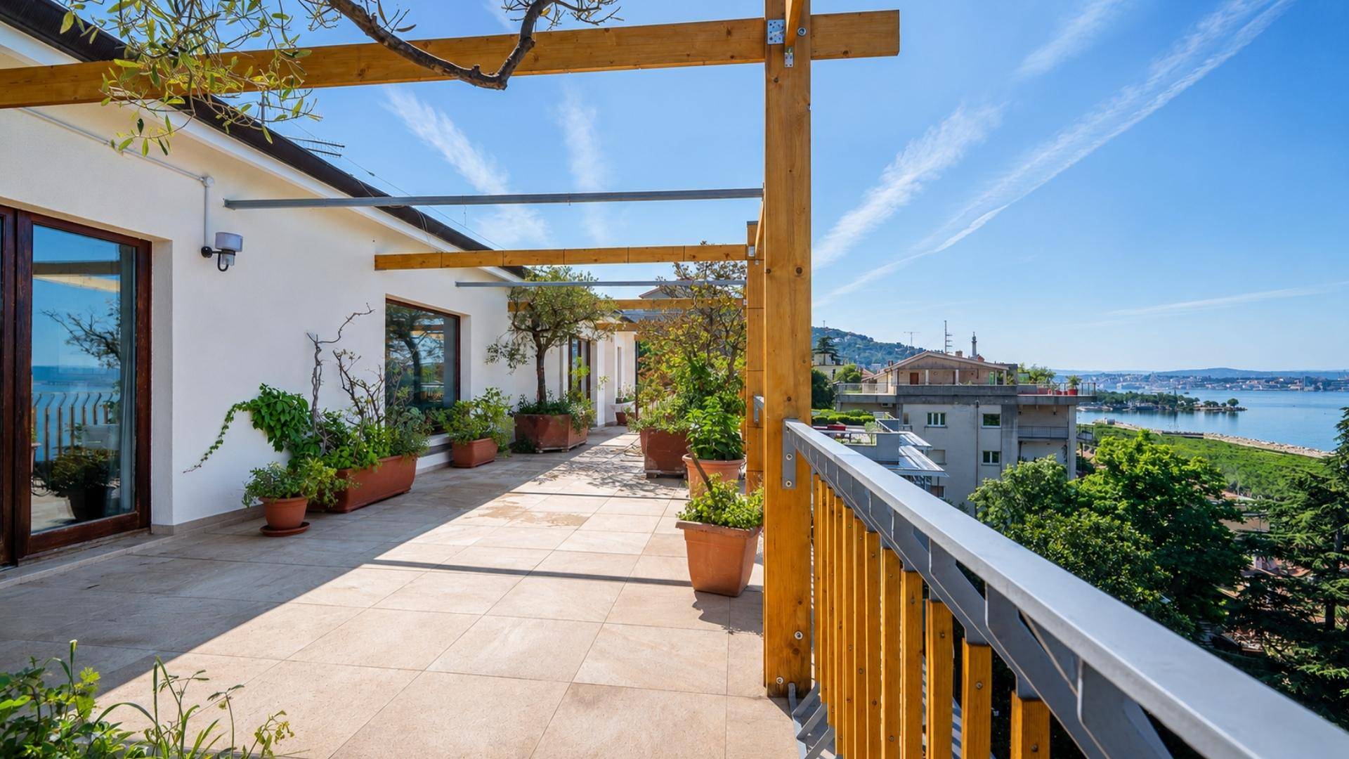 Lange Terrasse mit großen Glastüren, Pflanzen und weitem Blick auf das Meer und die Umgebung.