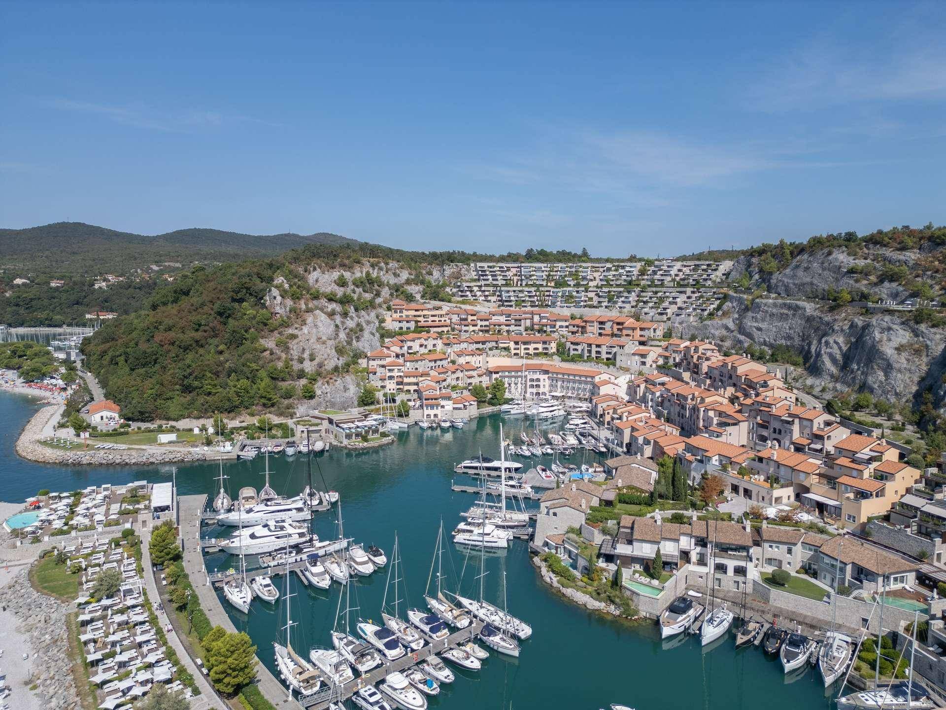 Panoramablick auf eine Küstensiedlung mit Yachthafen und terrassierten Gebäuden.