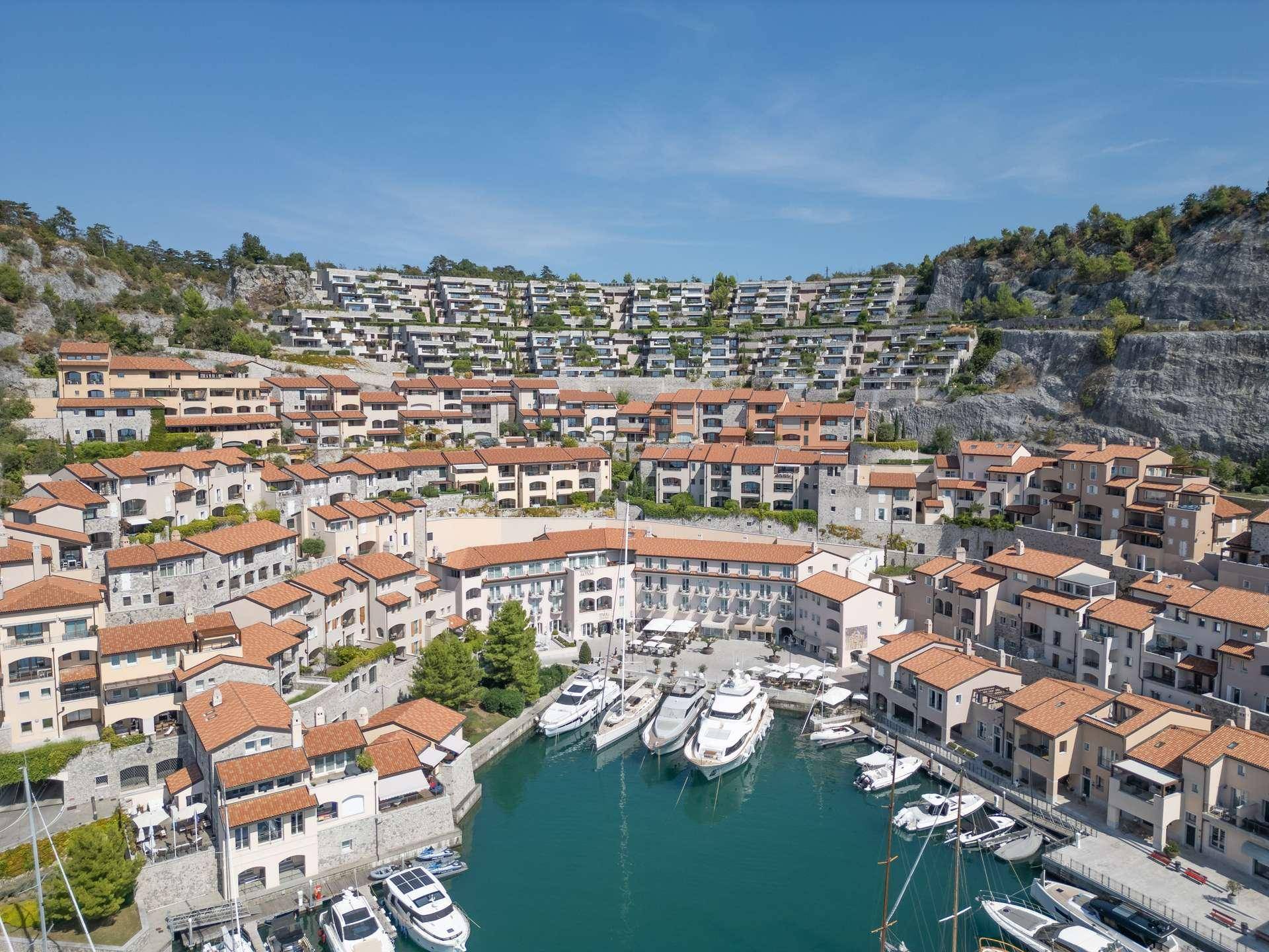 Weitläufige Ansicht einer Küstensiedlung mit terrassierten Häusern und einem belebten Hafen.