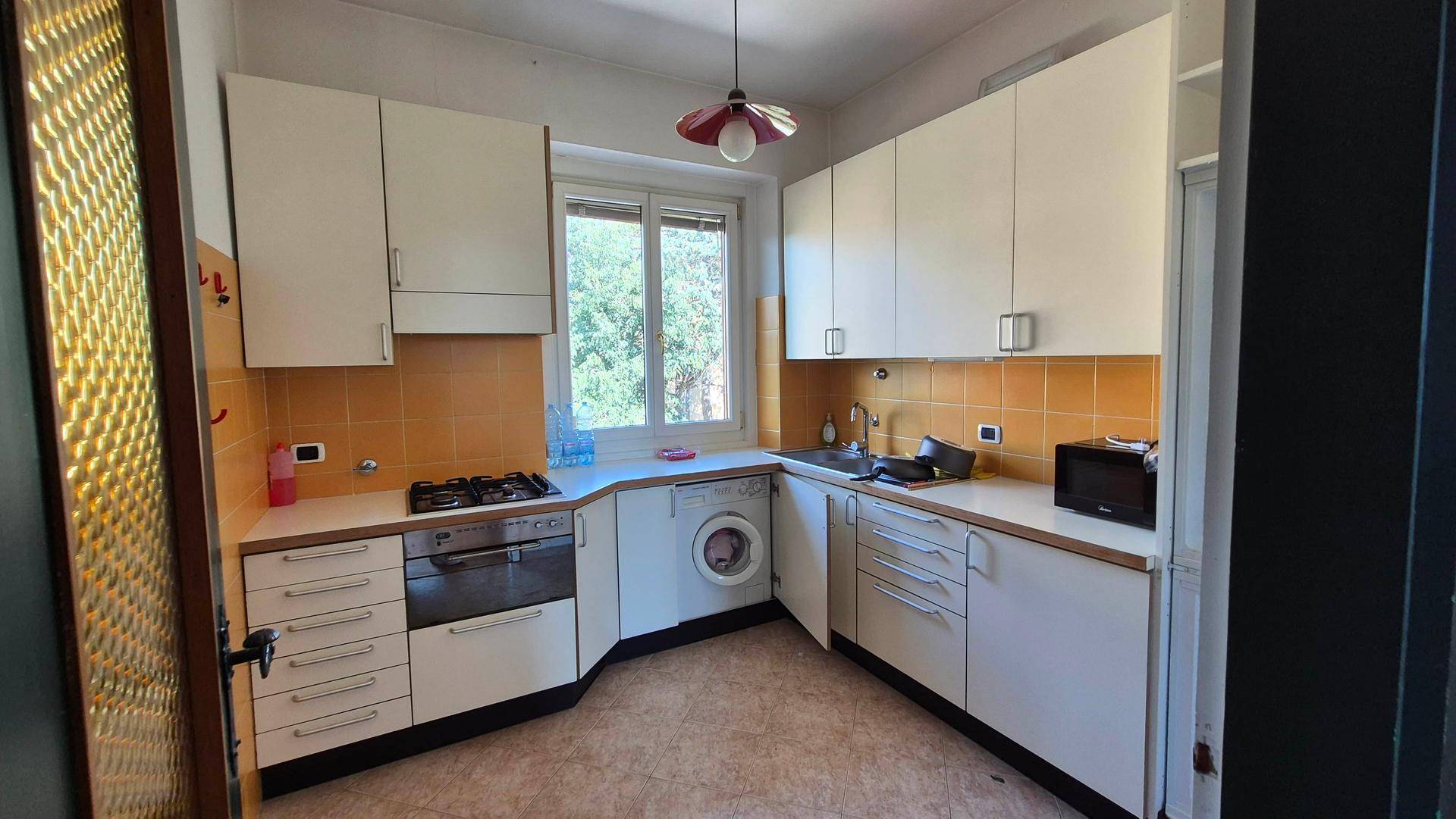 Funktionale Küche mit weißen Schränken, gelben Fliesen, Fenster und integrierten Geräten.