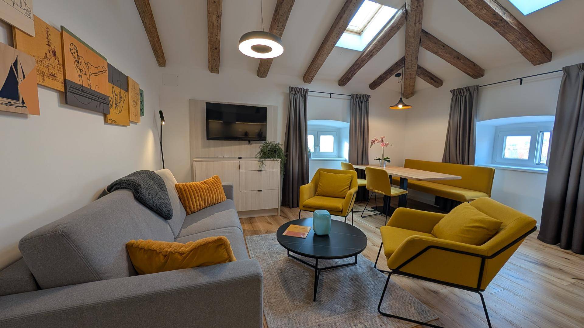 Gemütlicher Wohnbereich mit bequemen Sofas, gelben Akzentstühlen und Holzbalkendecke.