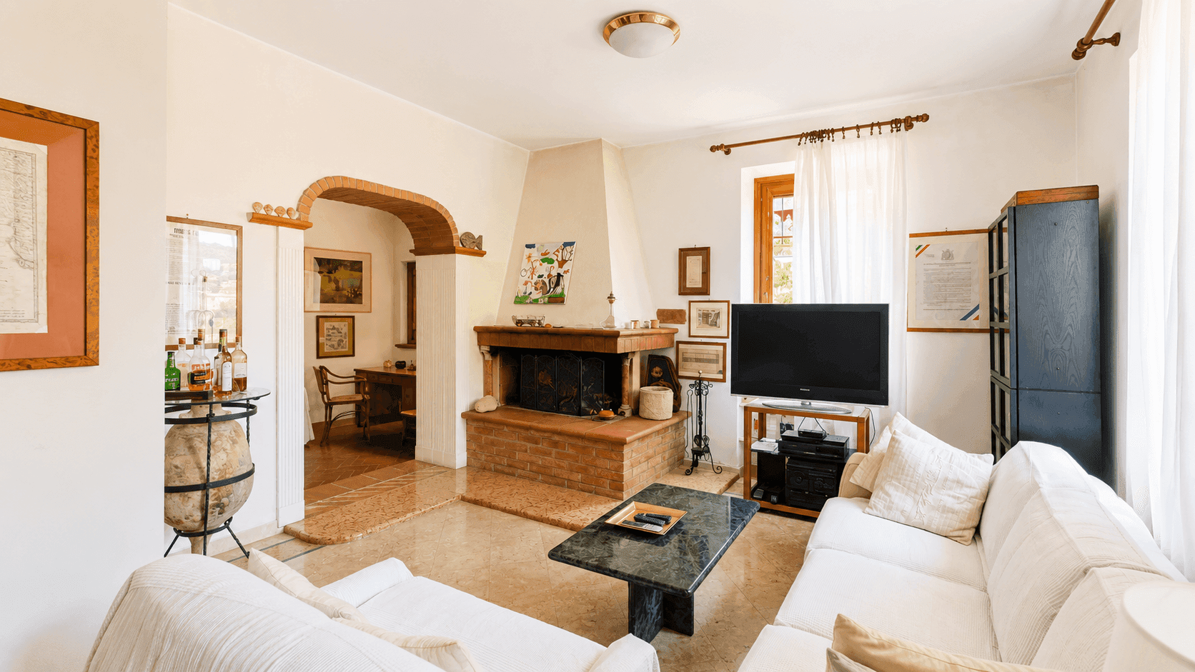 Geräumiges Wohnzimmer mit Kamin, hellen Sofas und Terrakottafliesen, offen zum Essbereich.