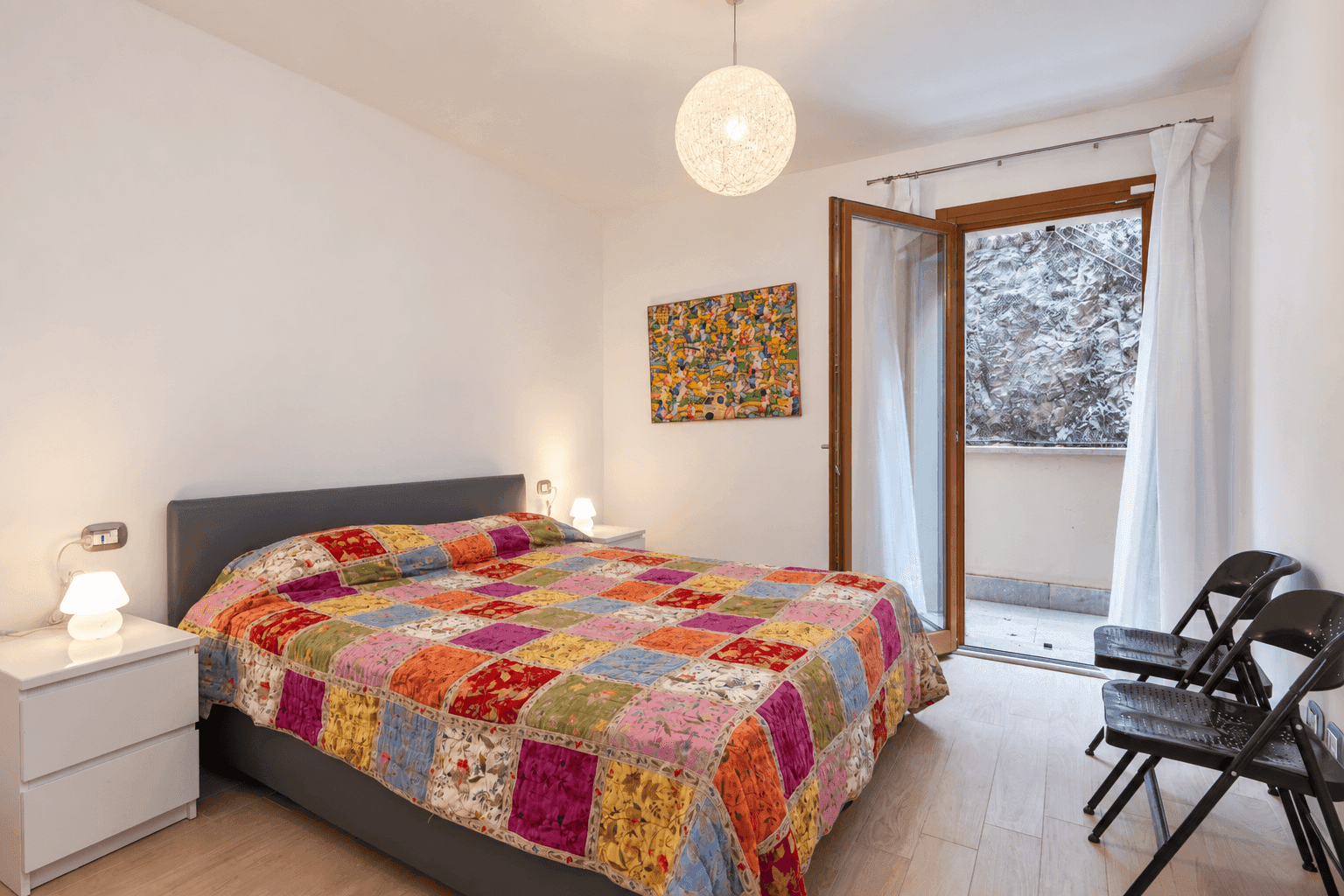 Gemütliches Schlafzimmer mit farbenfroher Bettdecke und Zugang zu einem kleinen Balkon.