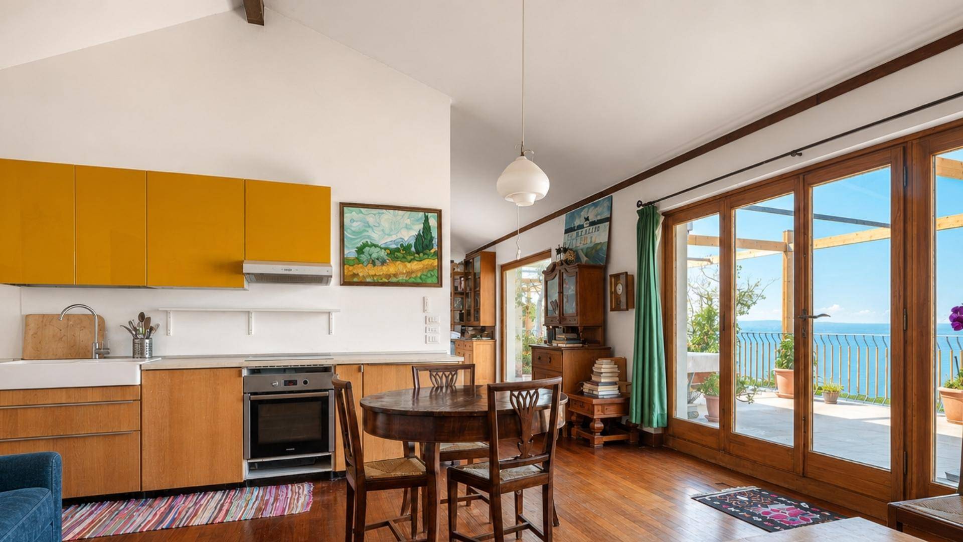 Offener Wohn-Essbereich mit integrierter Küche, Holzboden und Zugang zur Terrasse mit Meerblick.