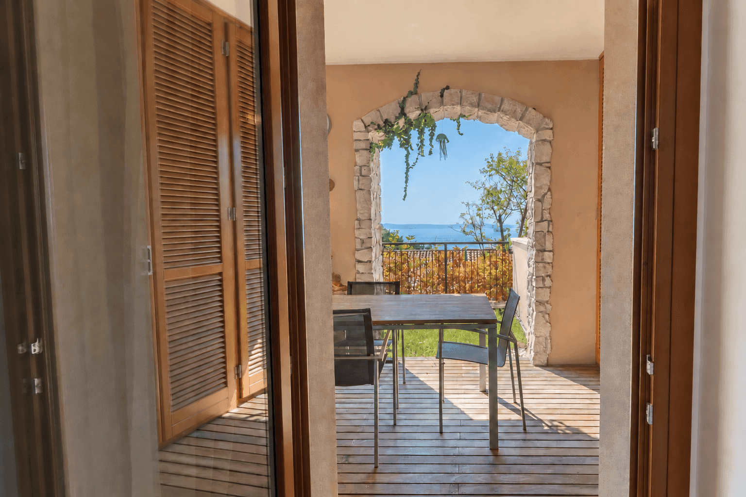 Überdachte Terrasse mit Esstisch und Meerblick durch einen dekorativen Steinbogen.