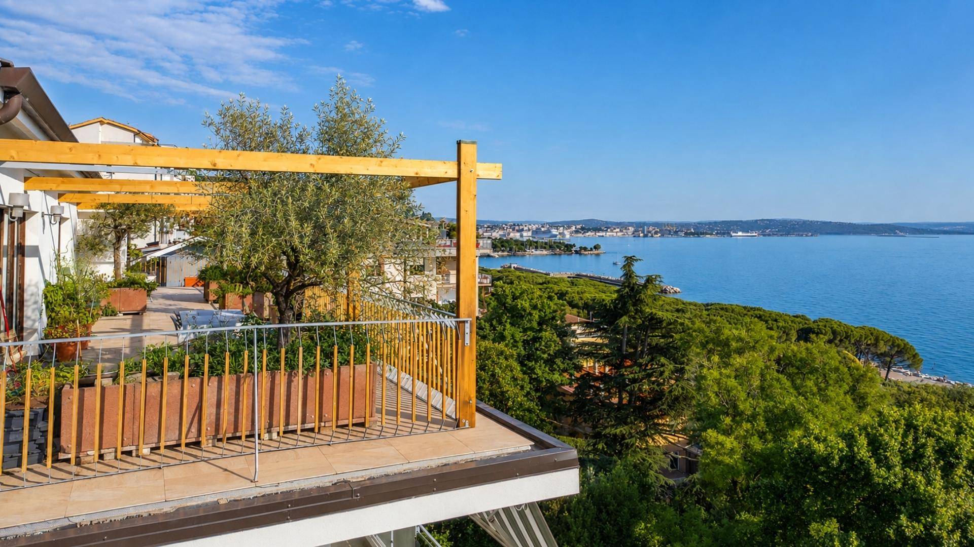 Terrasse mit weitem Blick auf das Meer und die grüne Küstenlandschaft unter blauem Himmel.