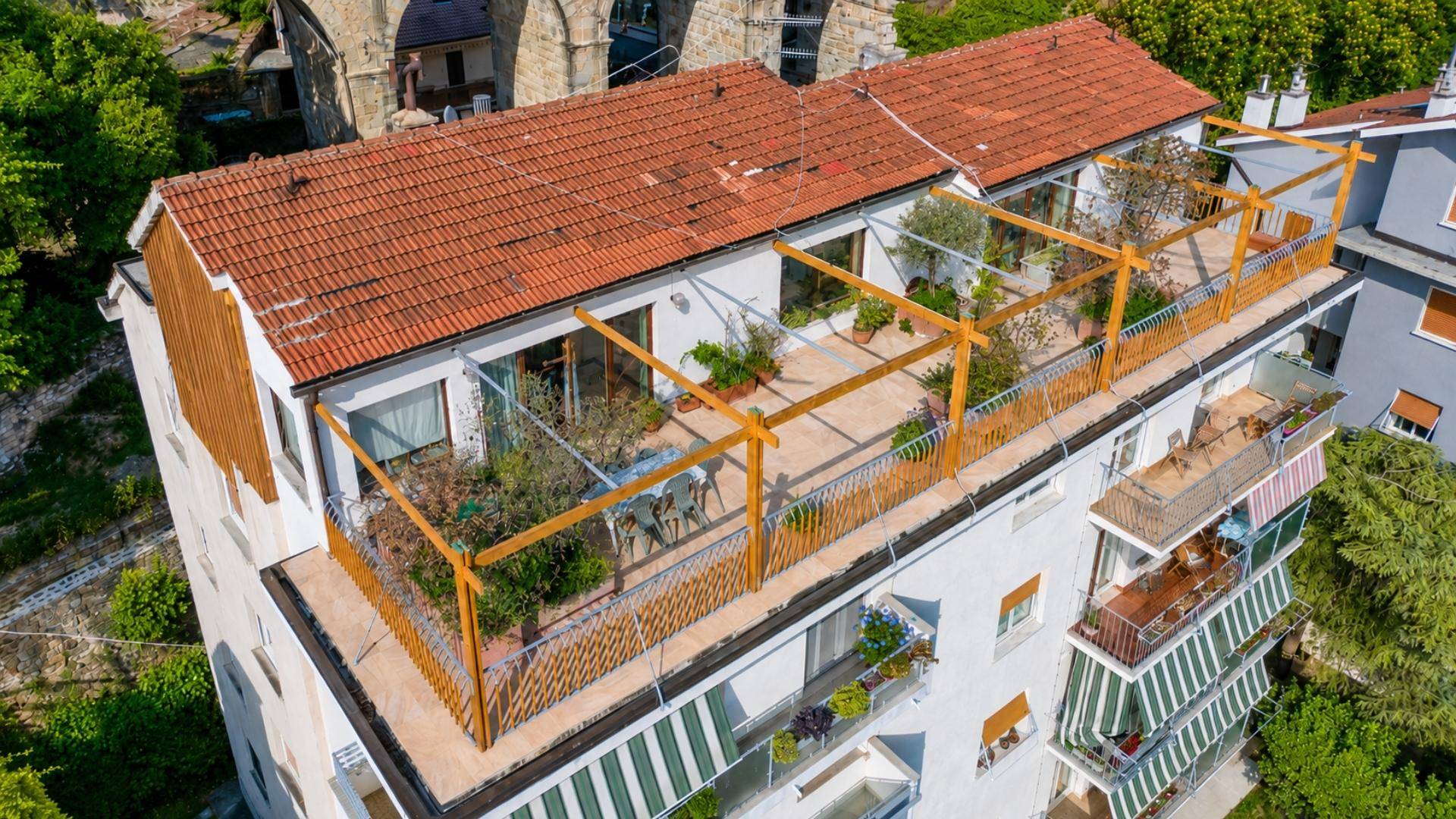 Luftaufnahme des Gebäudes mit großer Dachterrasse und Pergola, umgeben von grüner Landschaft.