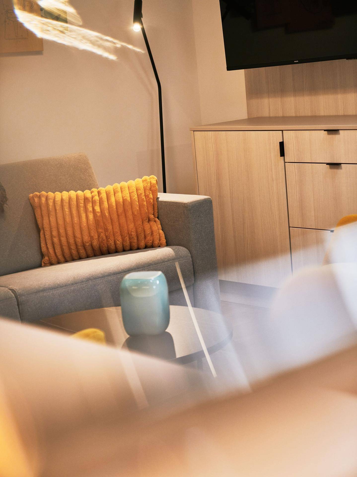 Detailaufnahme des Wohnbereichs mit grauem Sofa, gelbem Kissen und modernem Beistelltisch.