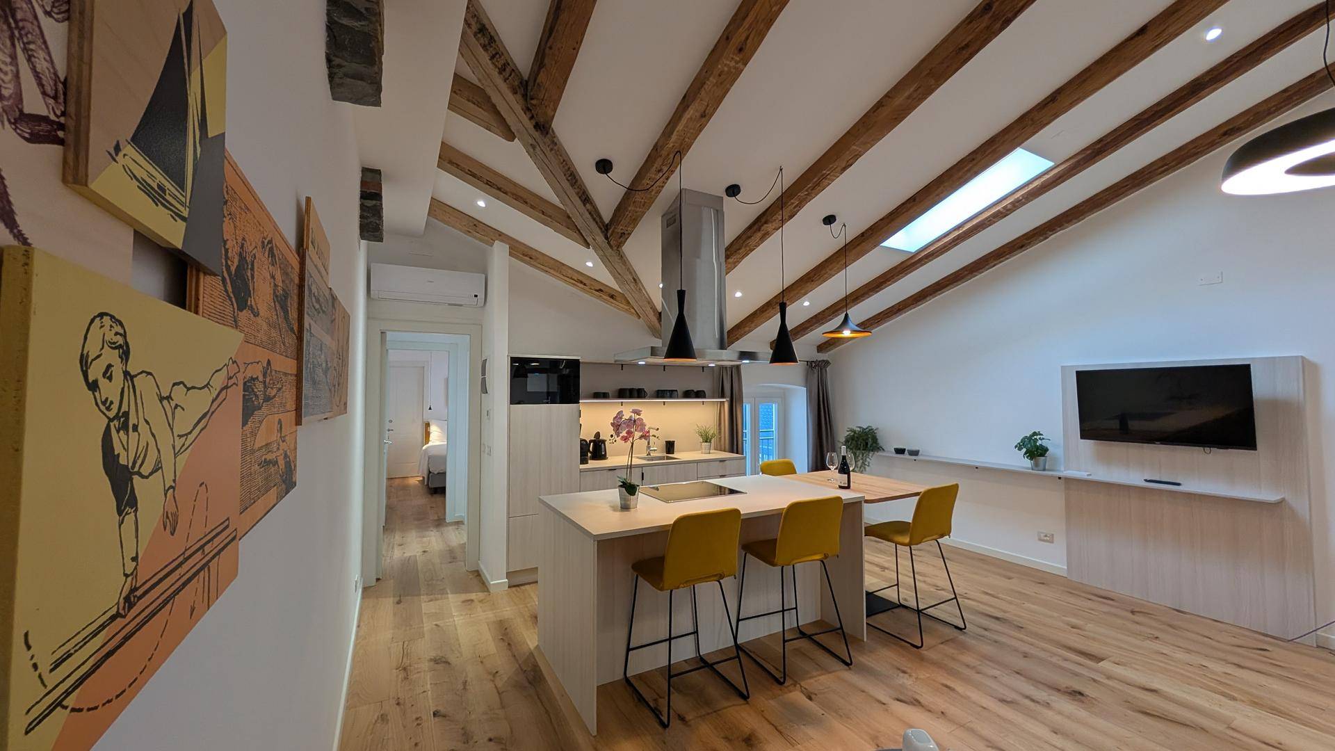 Heller Wohnbereich mit offener Küche, sichtbaren Holzbalken, großen Dachfenstern und moderner Einrichtung.