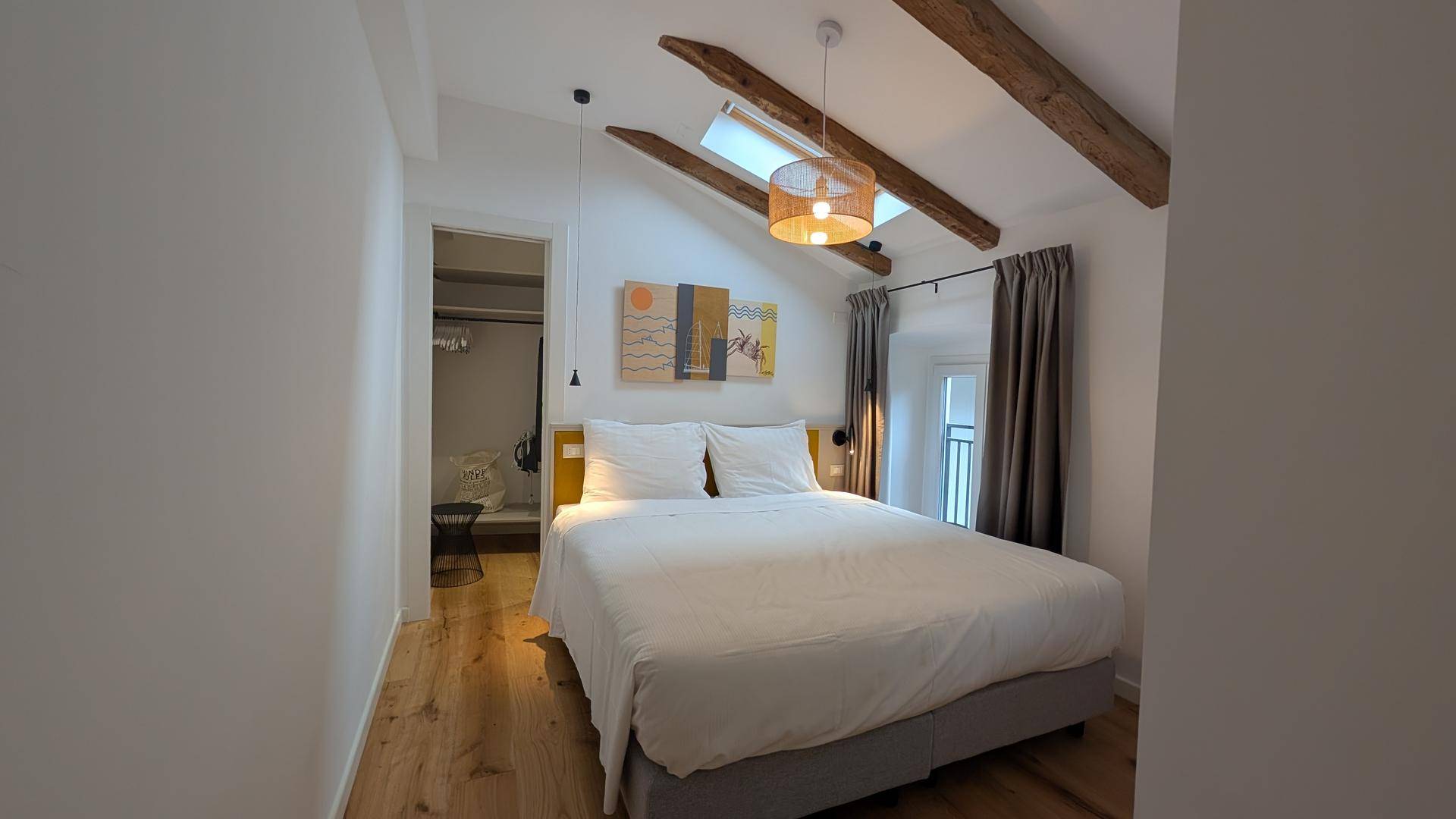 Gemütliches Schlafzimmer mit Doppelbett, Holzbalken, Dachfenster und Zugang zu einem Ankleidebereich.