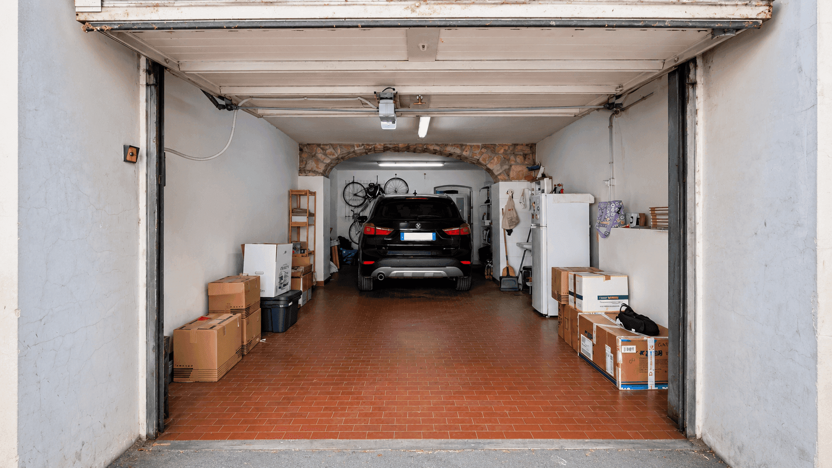 Geräumige Garage mit einem Auto, Lagerregalen und Kartons, die zusätzlichen Stauraum bieten.
