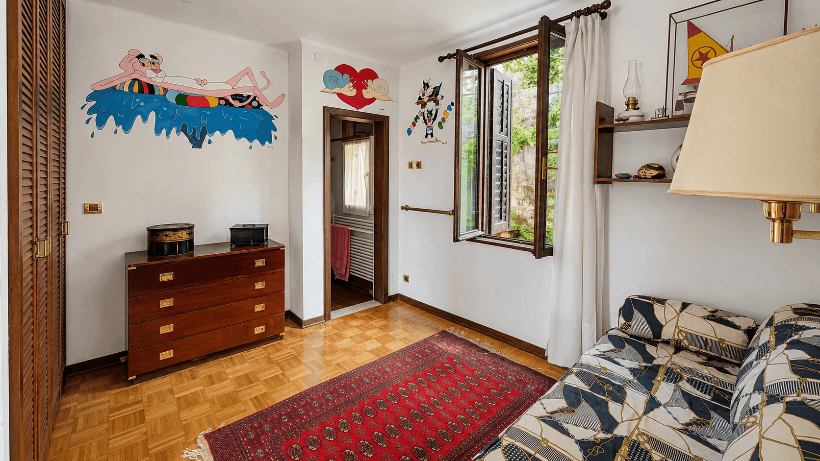 Kinderzimmer mit Parkettboden, farbenfroher Wanddekoration und Fenster mit Blick ins Grüne.