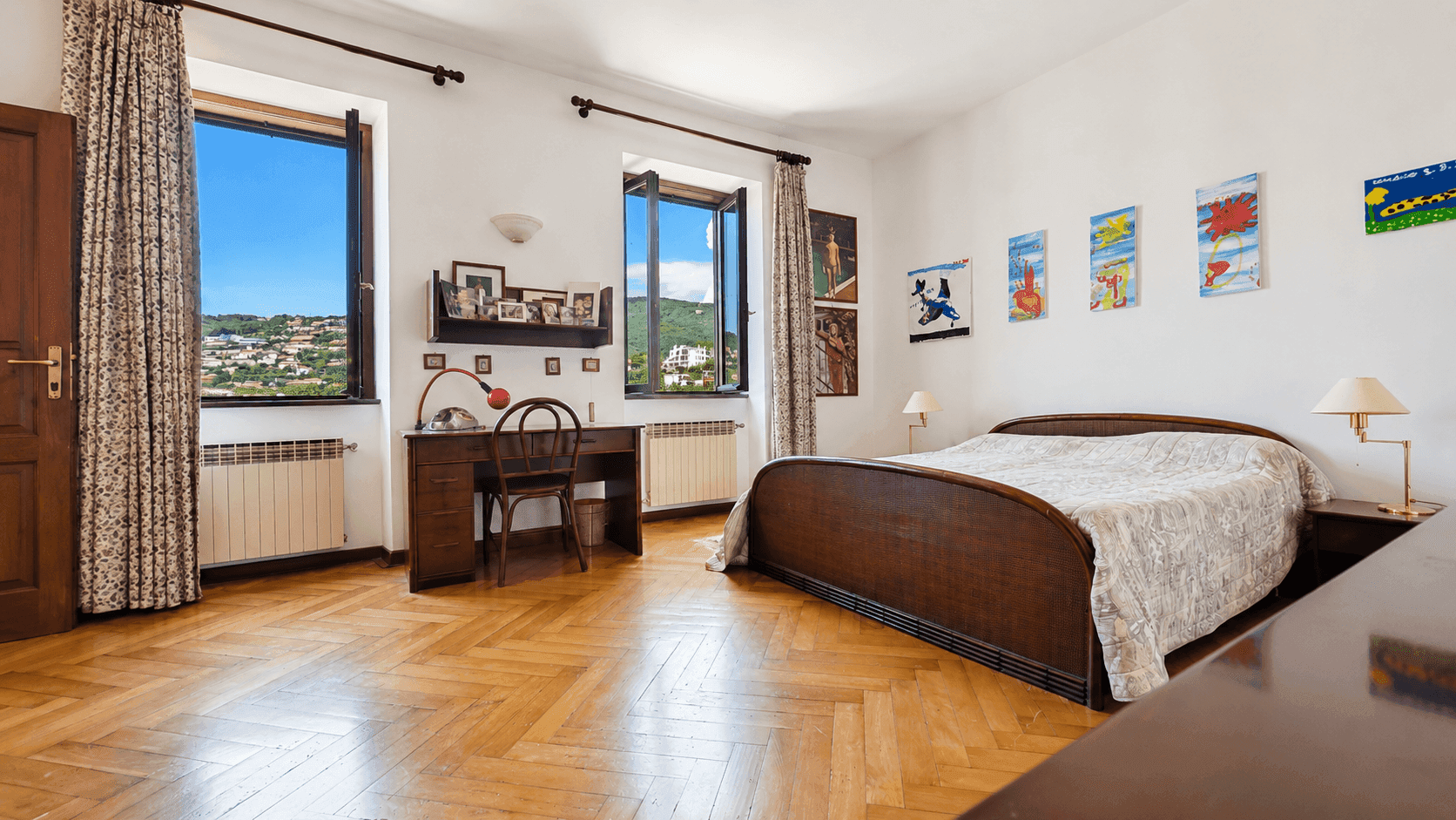 Helles Schlafzimmer mit Holzparkett, Schreibtisch und Fenstern, die einen weiten Blick bieten.