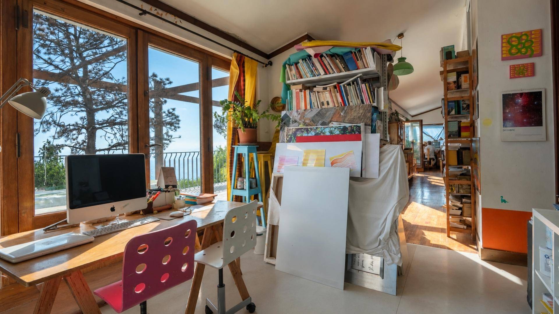Arbeitszimmer mit Schreibtisch, Bücherregalen und weitem Blick auf Bäume und das Meer.