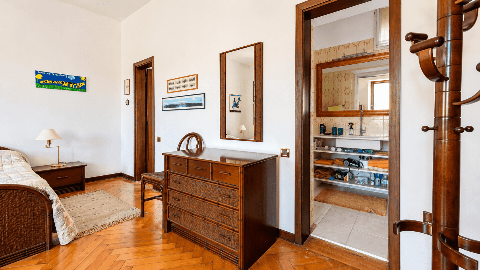Helles Schlafzimmer mit Holzparkett, Kommode und direktem Zugang zu einem Badezimmer.