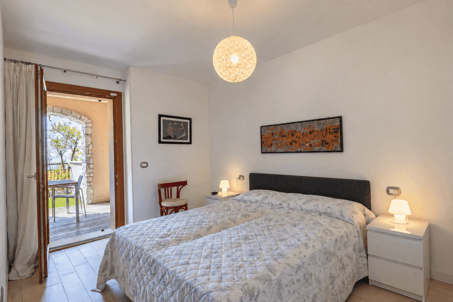 Helles Schlafzimmer mit Doppelbett, Nachttischen und Zugang zur Außenterrasse.