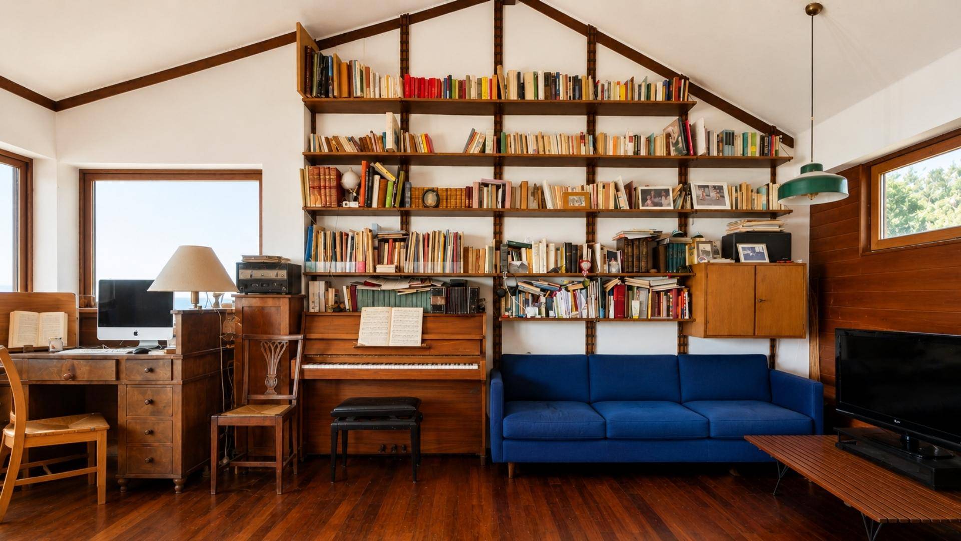Wohnzimmer mit blauer Couch, Klavier und raumhohen Bücherregalen, die zum Lesen einladen.
