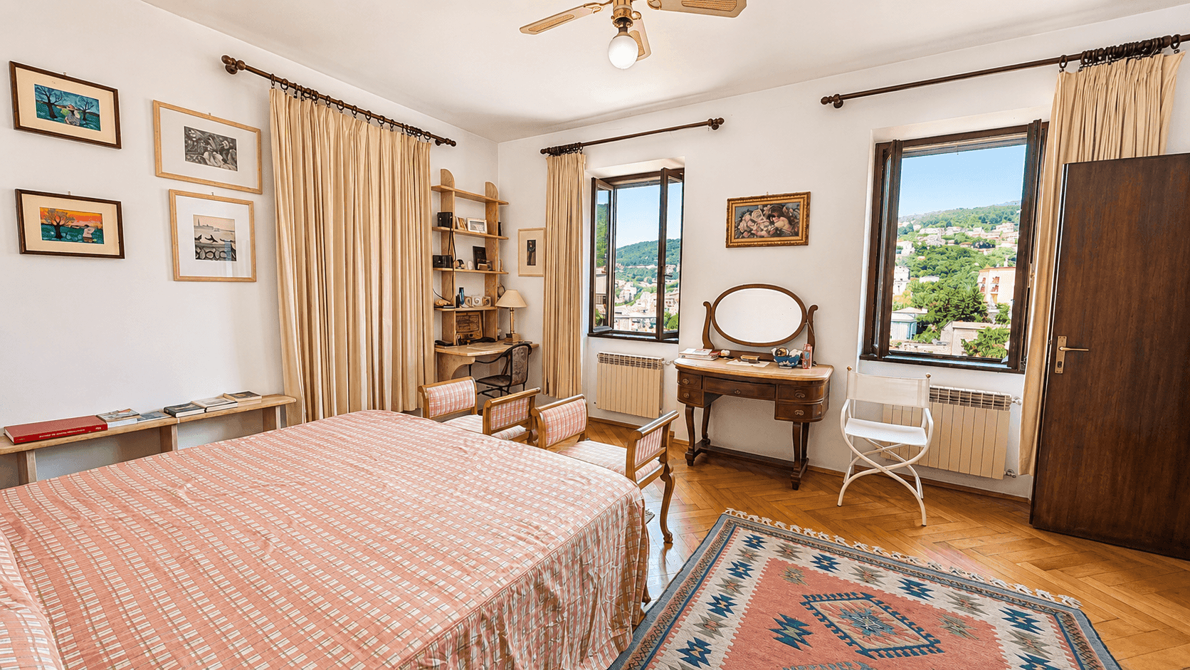 Helles Schlafzimmer mit Parkettboden, Schminktisch und Deckenventilator, bietet einen weiten Ausblick.