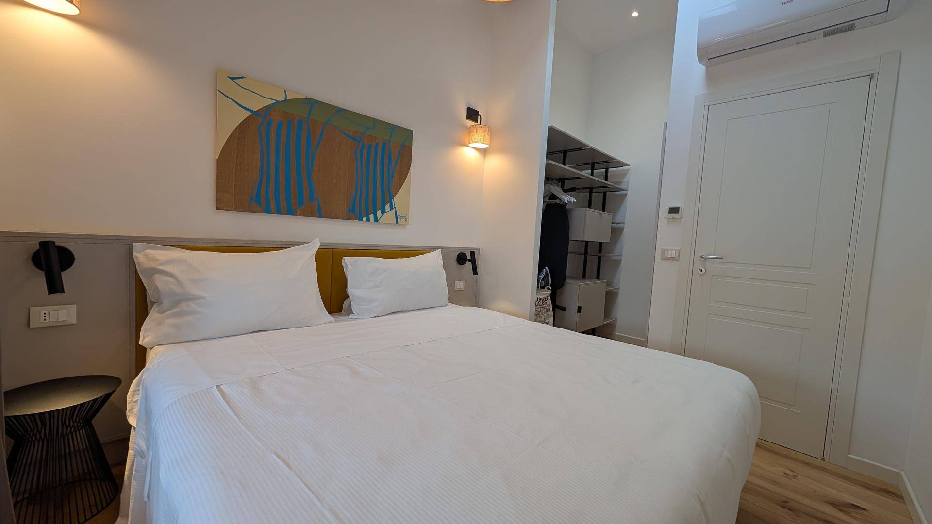 Helles Schlafzimmer mit Doppelbett, offener Garderobe und Klimaanlage.