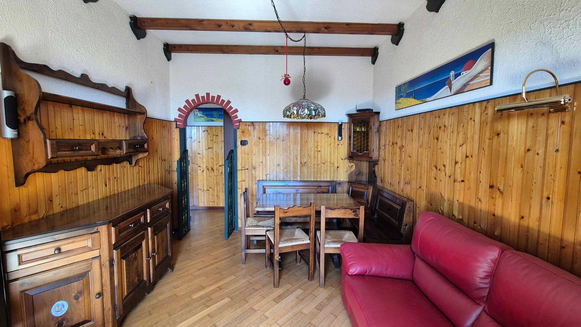Traditioneller Wohn- und Essbereich mit Holzvertäfelung, Holzbalken, rotem Sofa und Esstisch.
