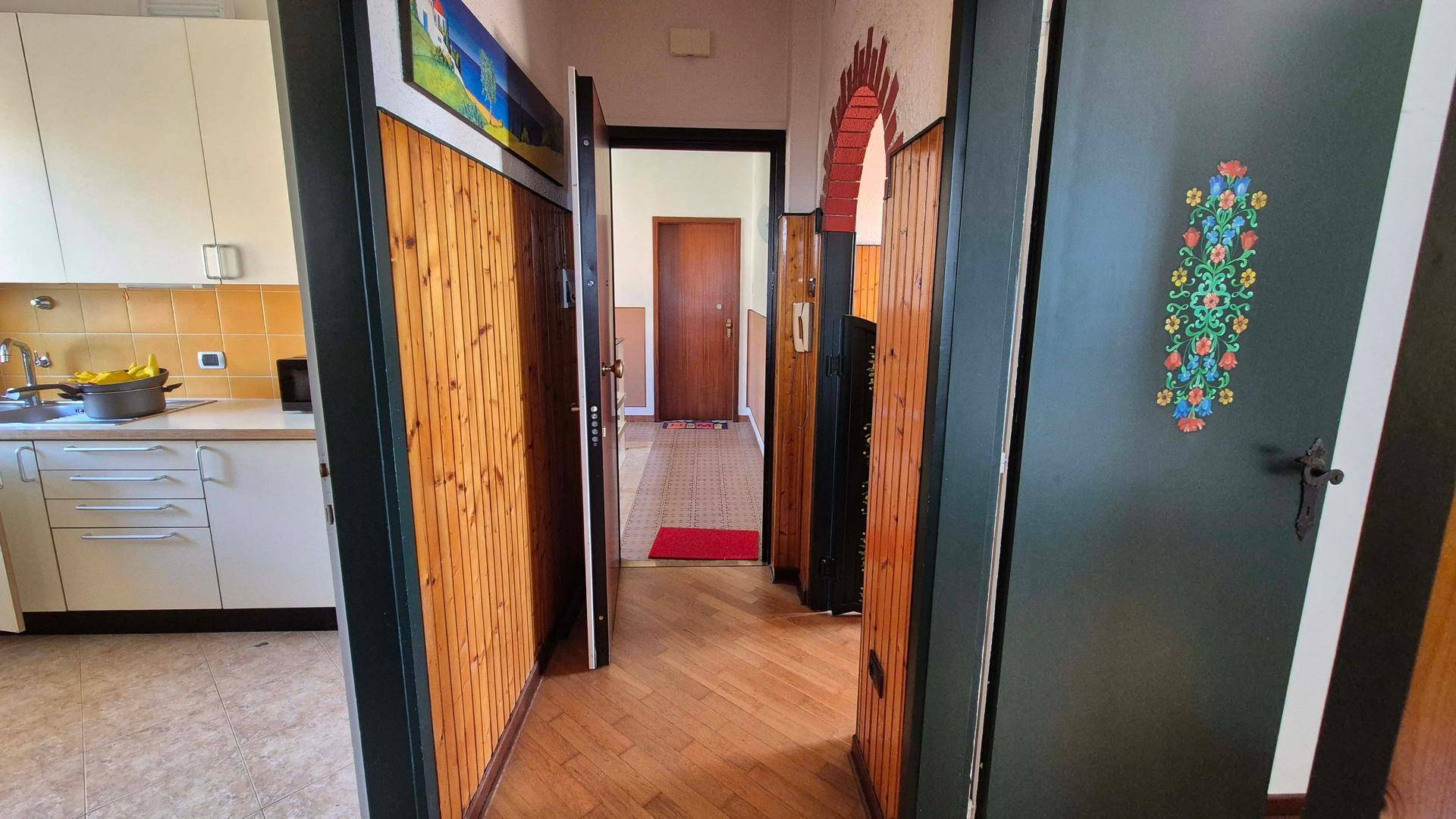 Gemütlicher Flur mit Holzvertäfelung und Blick in eine angrenzende Küche mit gelben Fliesen.