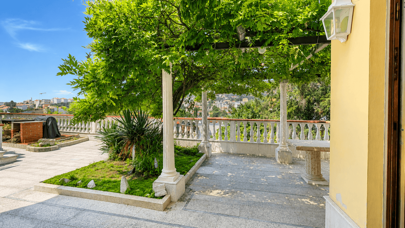 Geräumige Terrasse mit Pergola, Säulen und einem üppigen Baum, ideal für entspannte Stunden im Freien.