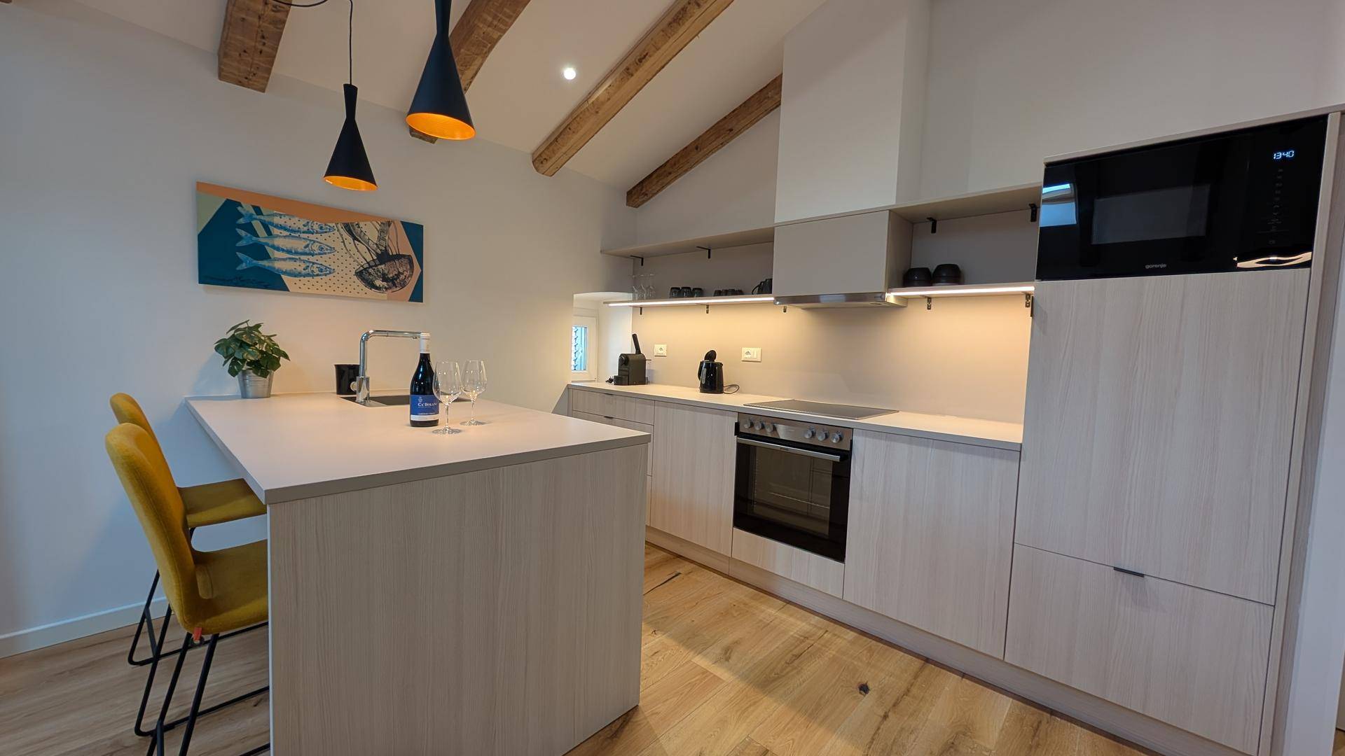 Helle Küche mit Kücheninsel, modernen Geräten und Holzbalkendecke in offenem Raumkonzept.