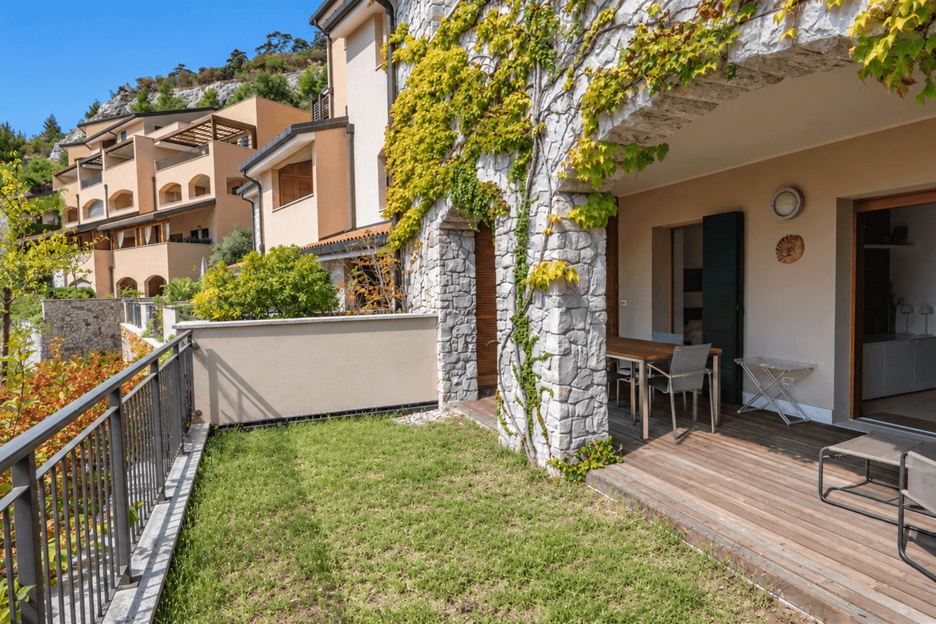 Gartenbereich mit Rasenfläche und Terrasse, umgeben von mediterraner Architektur.
