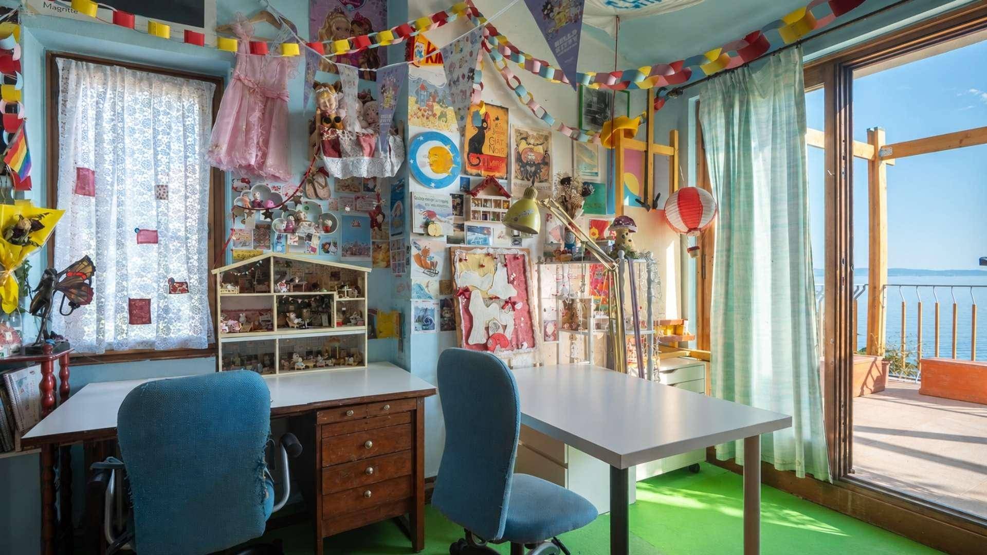 Helles Kinderzimmer mit Schreibtischen, bunten Dekorationen und Zugang zur Terrasse mit Meerblick.