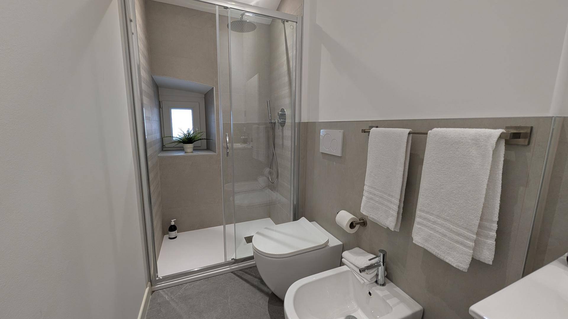 Modernes Badezimmer mit Duschkabine, WC, Bidet und beheiztem Handtuchhalter.