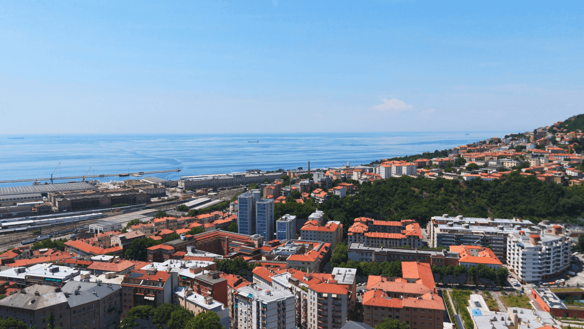 Panoramablick auf die Küstenstadt mit Hafen, Gebäuden und dem weiten Meer unter klarem Himmel.