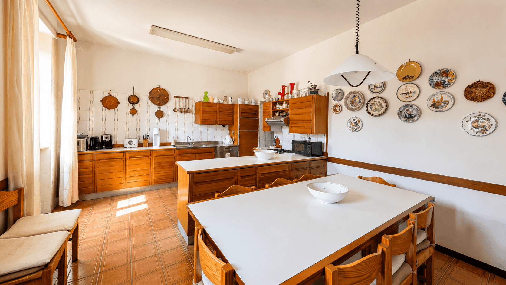 Geräumige Küche mit Holzschränken, großem Esstisch und Terrakottafliesen, ideal für Familienessen.