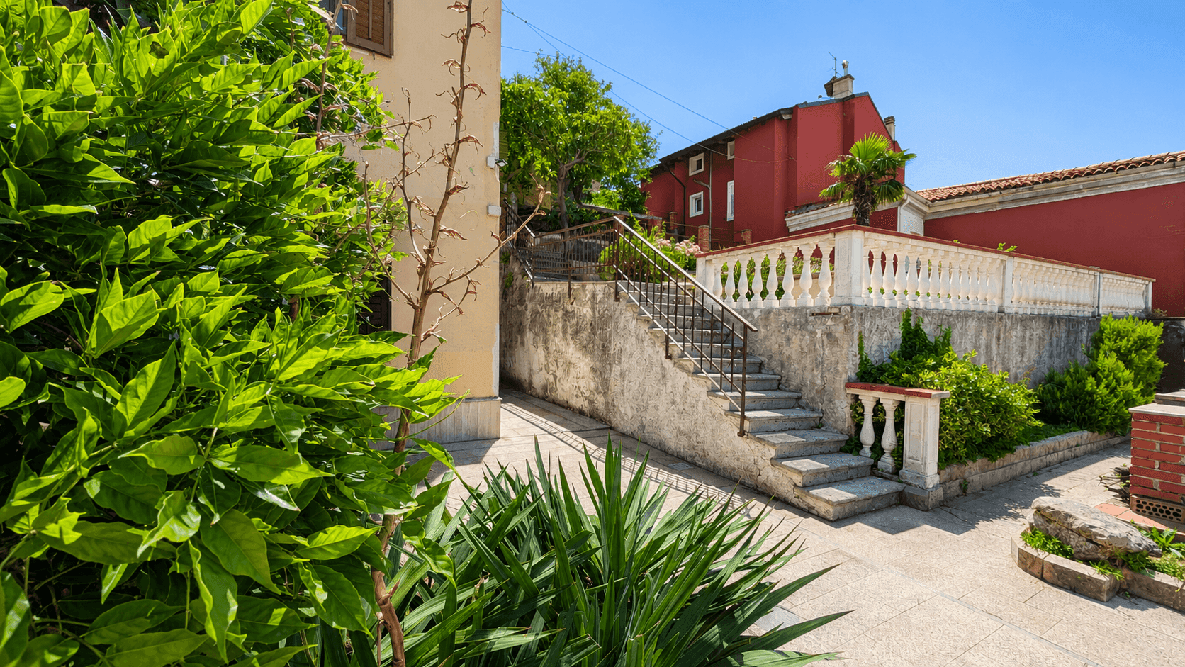 Außentreppe mit Balustrade und üppiger Vegetation, die zu verschiedenen Ebenen des Anwesens führt.