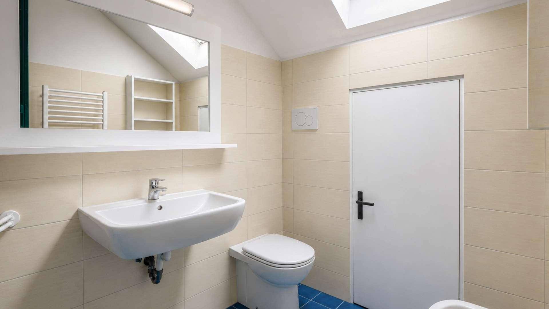Modernes Badezimmer mit beigefarbenen Fliesen, Waschbecken, Toilette und Dachfenster.