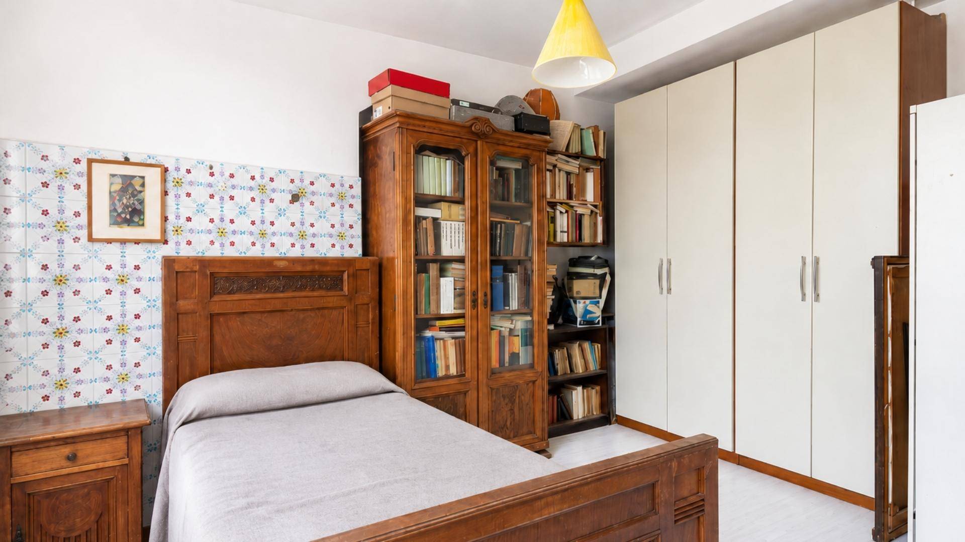 Schlafzimmer mit traditionellem Holzbett, Bücherregal und weißen Kleiderschränken.