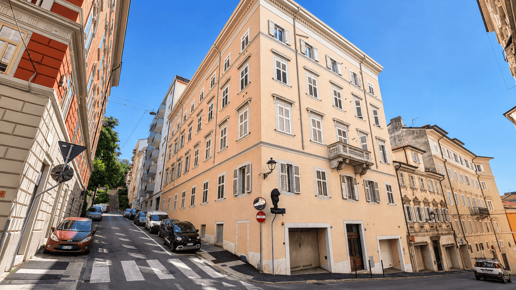 Historisches Gebäude an einer Straße mit vielen Fenstern und Balkonen, unter einem strahlend blauen Himmel.