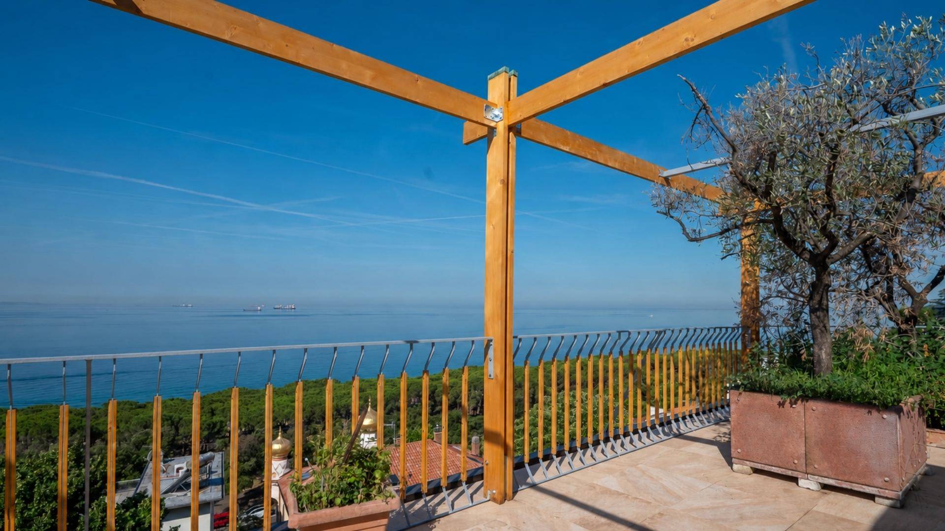 Weitläufige Terrasse mit Holzpergola und Panoramablick auf das weite Meer und die Küste.