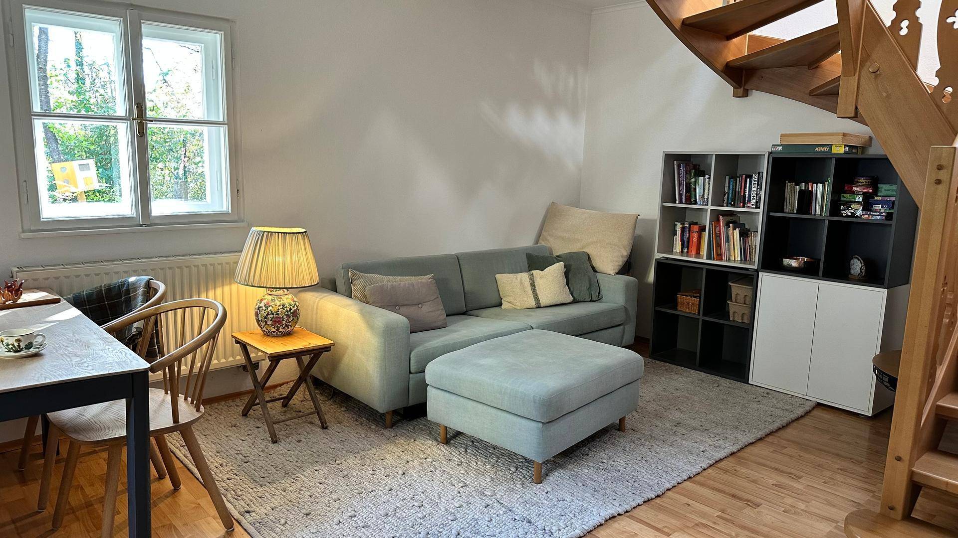 Gemütlicher Wohn- und Essbereich mit Sofa, Bücherregal und einer Holztreppe, die in die obere Etage führt.
