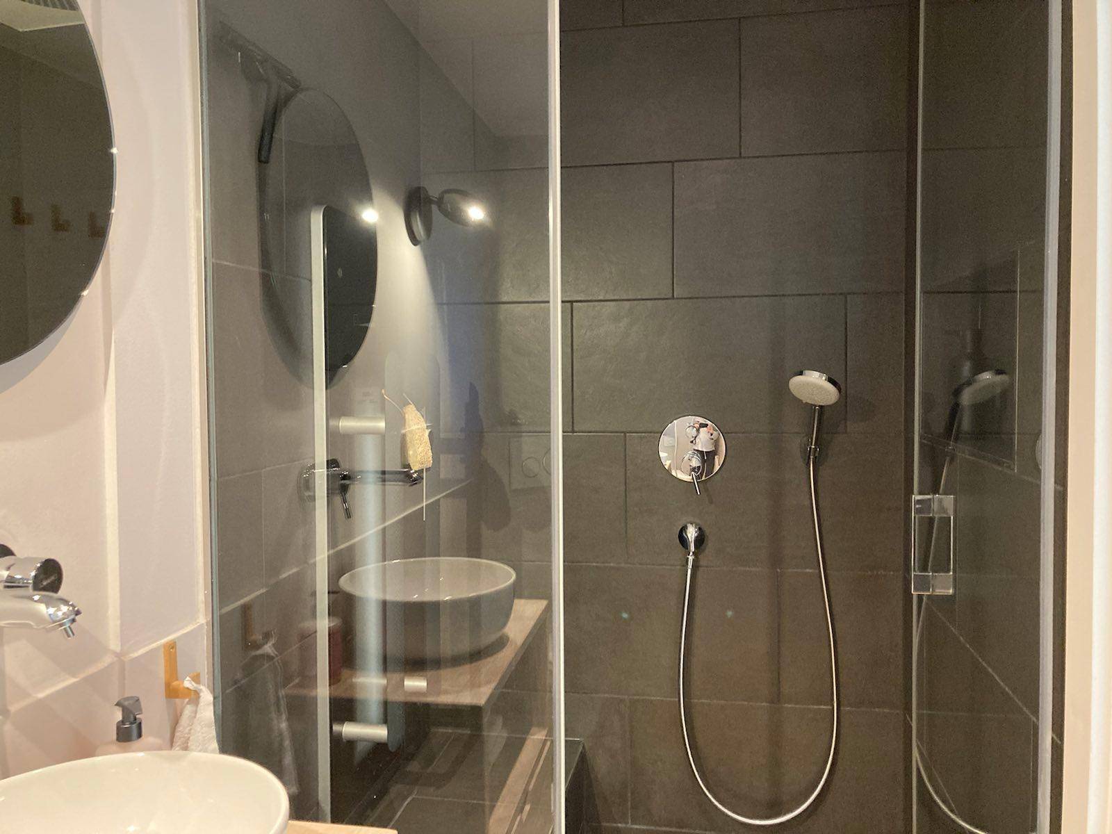 Elegantes Badezimmer mit begehbarer Dusche, dunklen Fliesen und modernem Design.