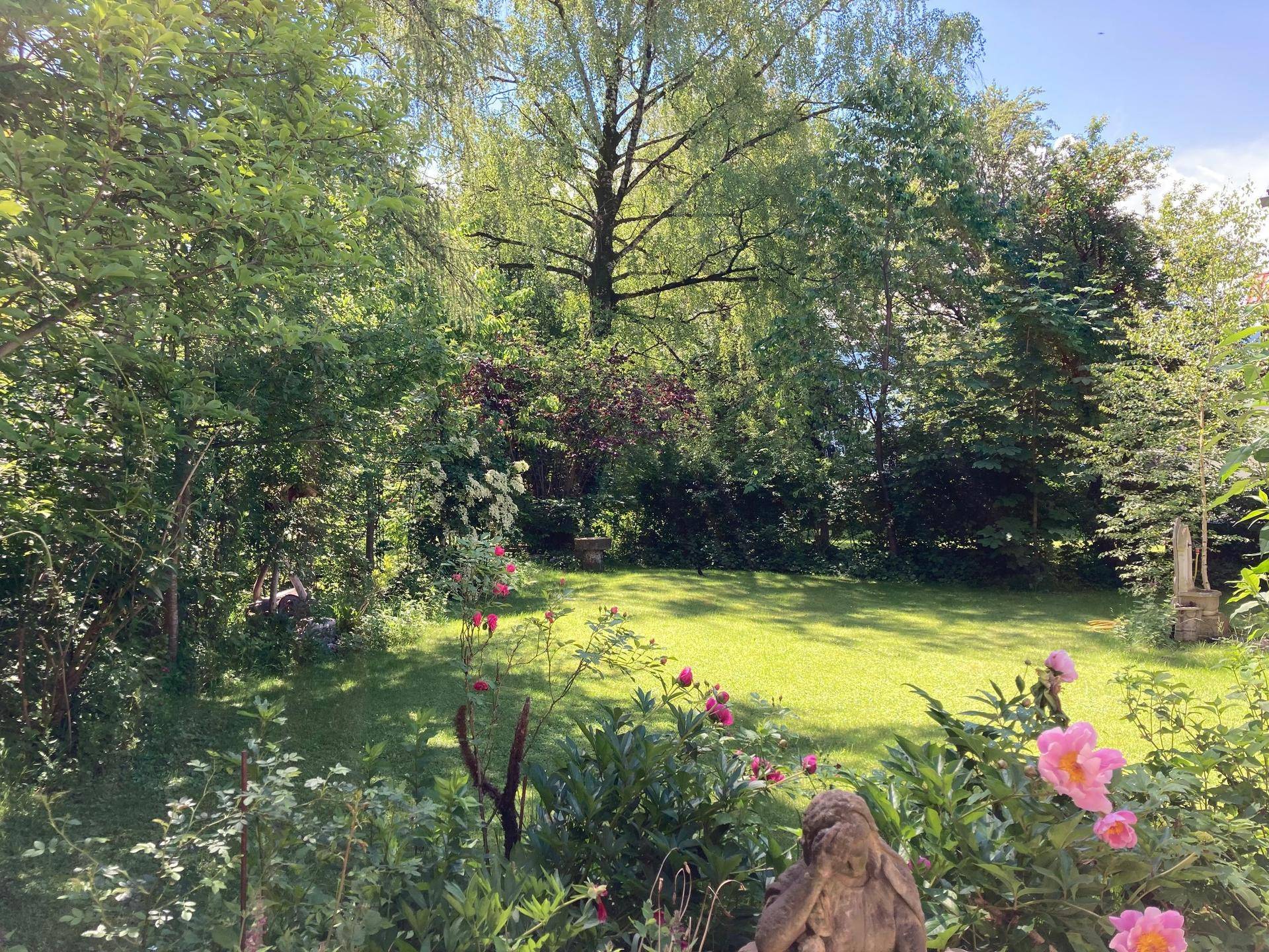 Gepflegter Garten mit Rasenfläche, blühenden Pflanzen und hohen Bäumen, ideal zum Entspannen im Freien.