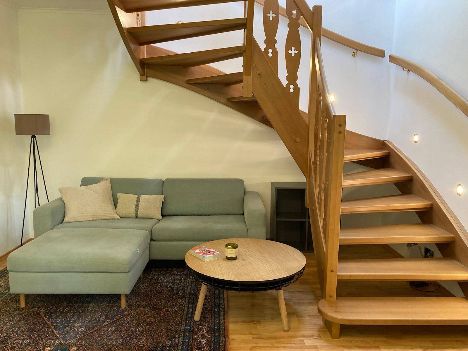 Wohnbereich mit einem bequemen Sofa, Couchtisch und einer eleganten Holztreppe mit integrierter Beleuchtung.
