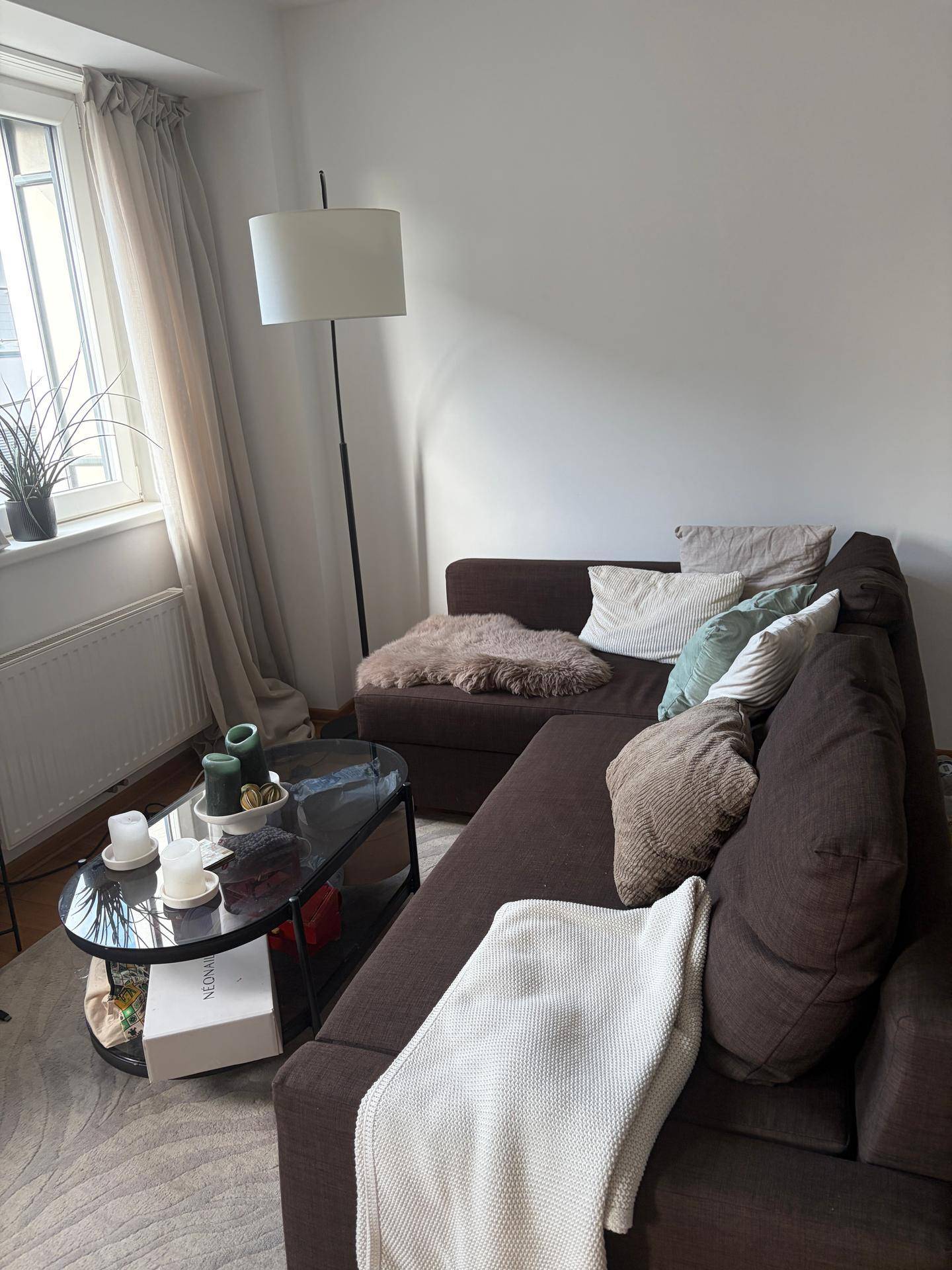 Gemütliches Wohnzimmer mit großem Ecksofa, Couchtisch und Stehlampe, hell durch das Fenster.