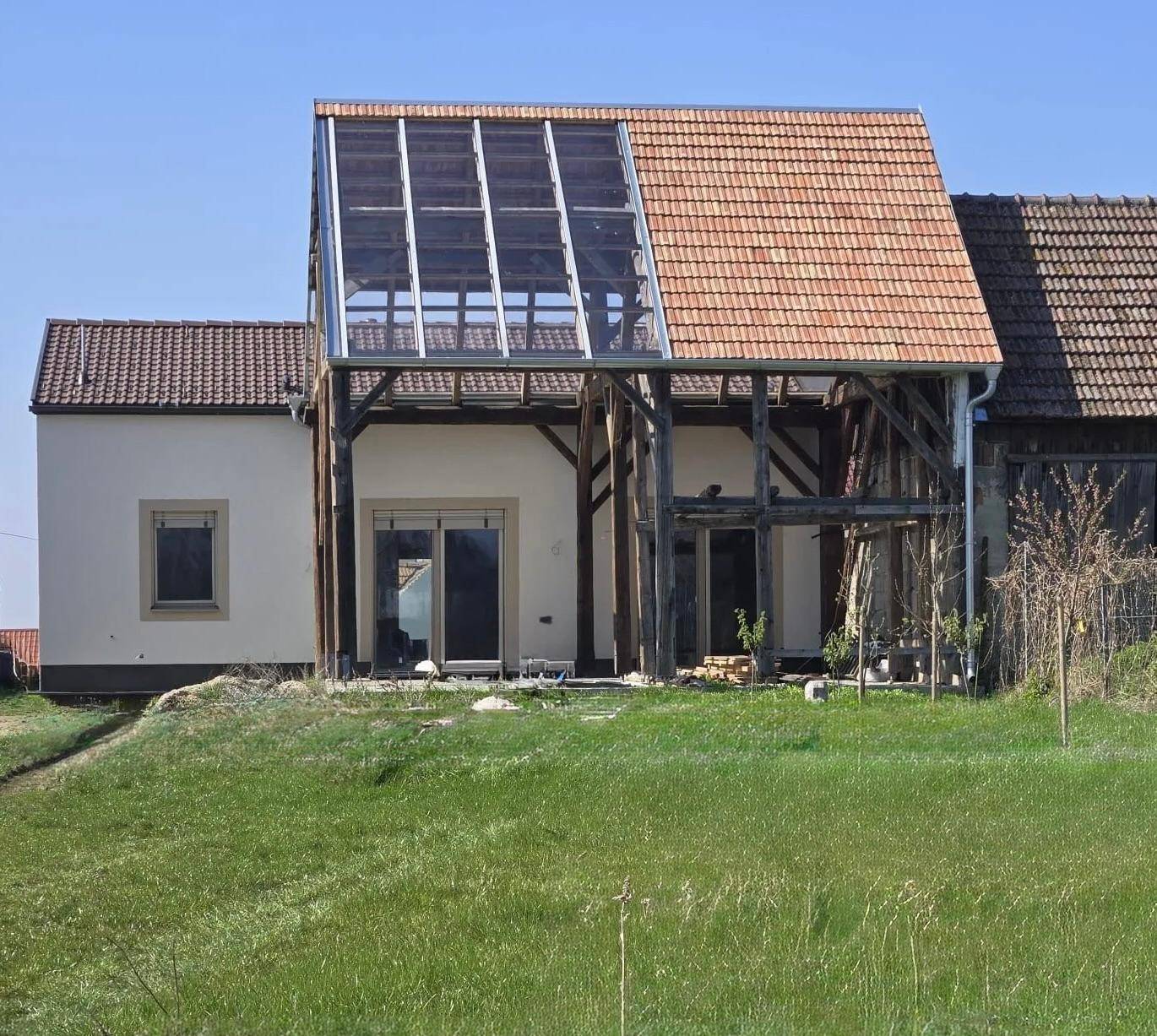 Historisches Gebäude mit moderner Glaserweiterung und traditionellem Ziegeldach in ländlicher Umgebung.