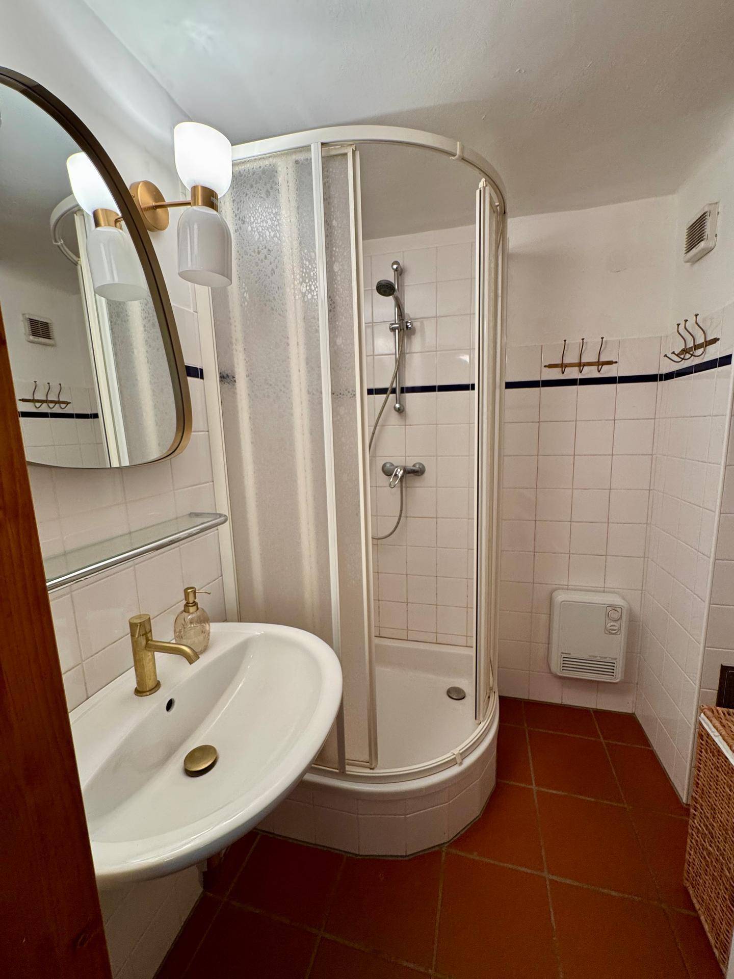 Kleines Badezimmer mit Duschkabine, Waschbecken und weißen Fliesen.